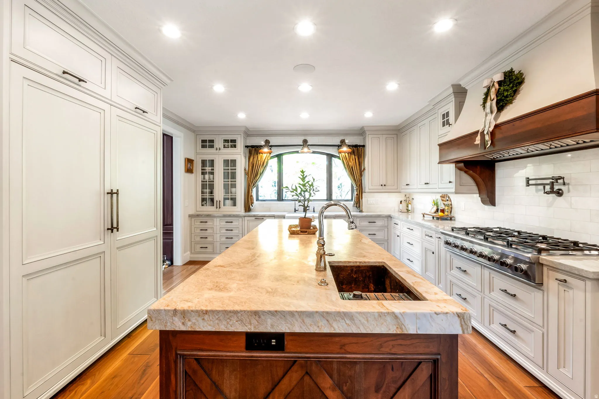 Spacious kitchen featuring an expansive center island with an undermount sink, built-in panel-ready refrigerator, stainless steel range with a pot filler, and white subway tile backsplash