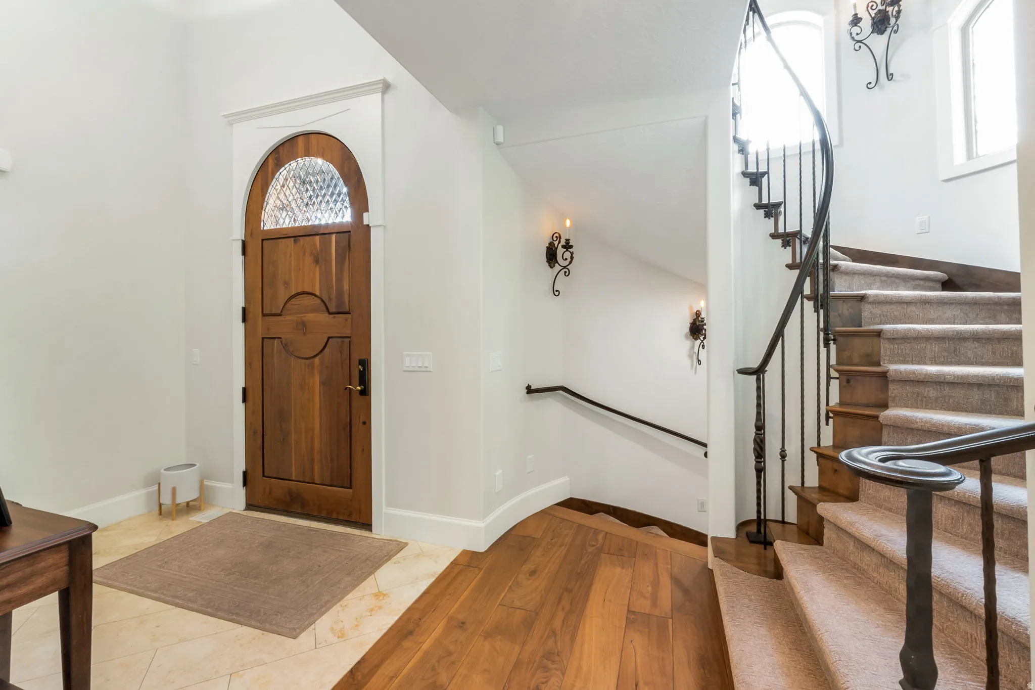 Wood-finish flooring and tile entryway featuring an arched wooden door with decorative glass