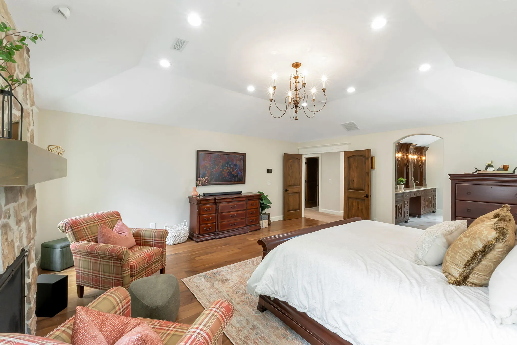 Spacious room featuring wood-finish flooring, a stone fireplace with a floating mantle, recessed lighting, and a decorative chandelier