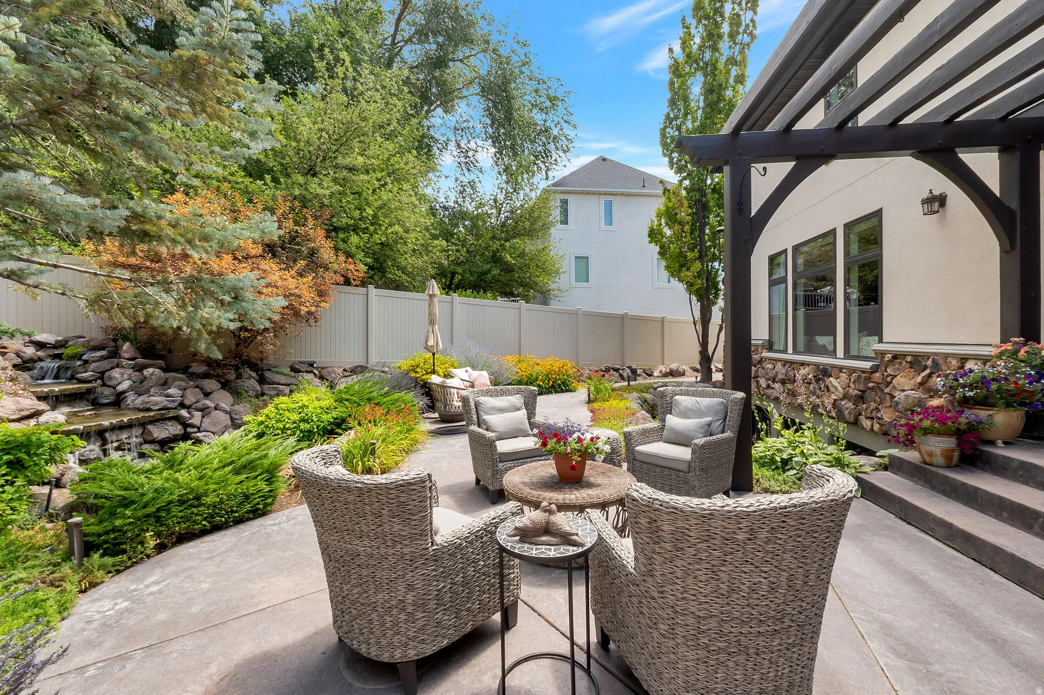 Patio area featuring a stone water feature, mature landscaping, a dark-stained wood pergola, stucco exterior, and stone veneer accents