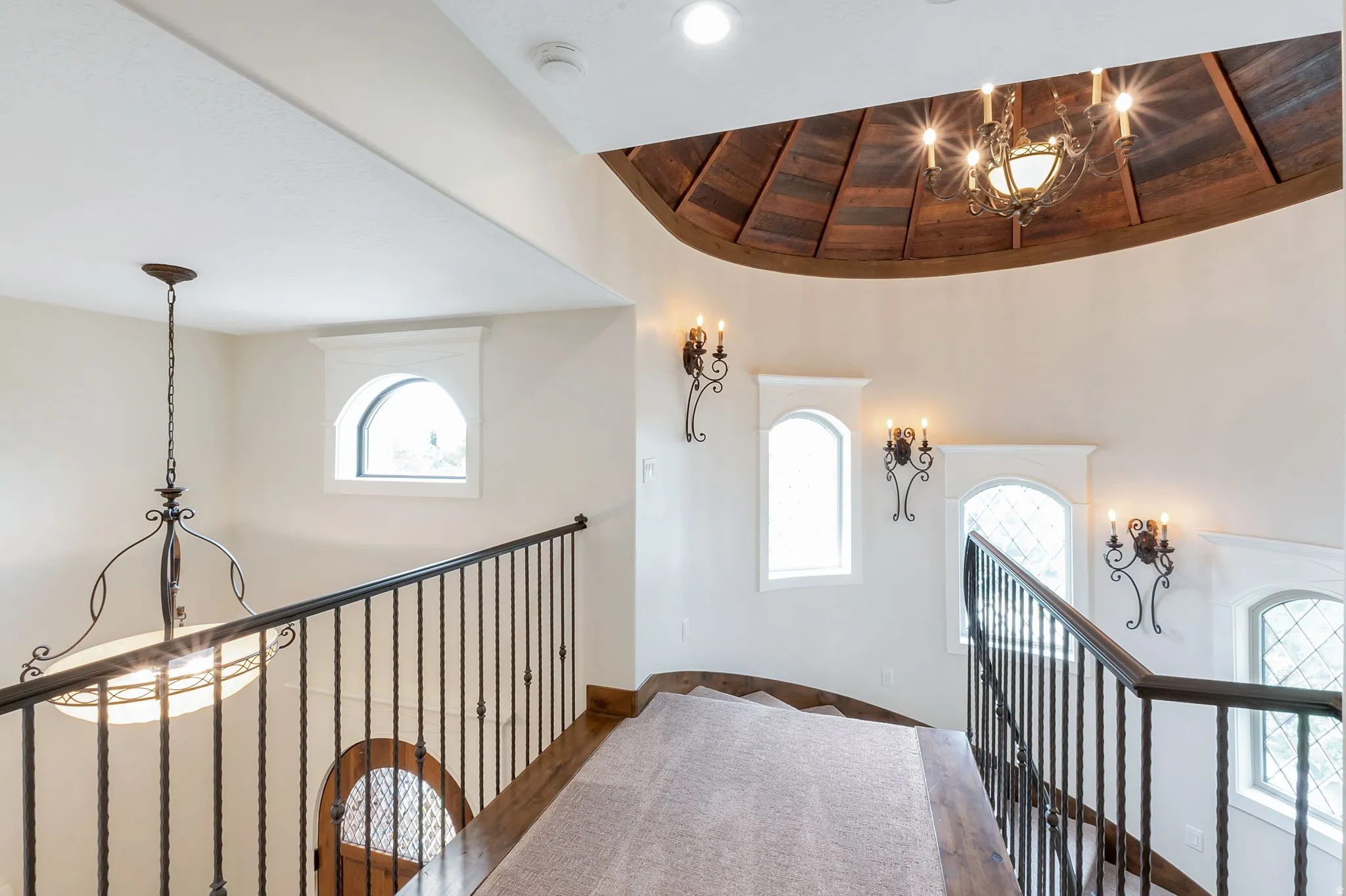Curved staircase featuring wrought iron railings, wood-finish flooring, and arched windows