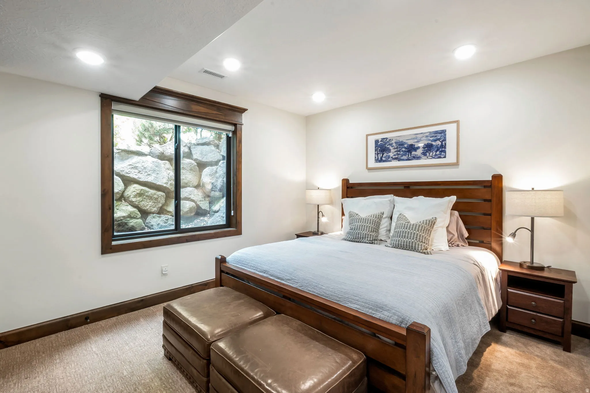 Recessed lighting illuminates this room featuring a window with substantial rock landscaping, wood-finish trim, and neutral carpeting