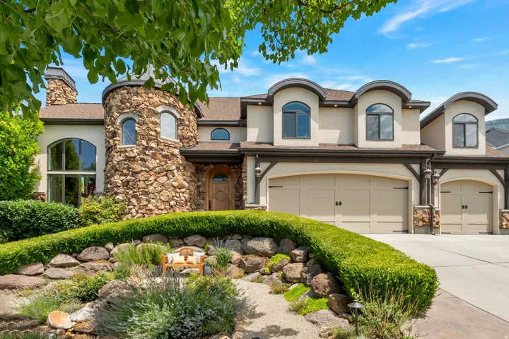 Stucco and stone exterior featuring a turret with arched windows, a wood entry door, and multiple dormer windows