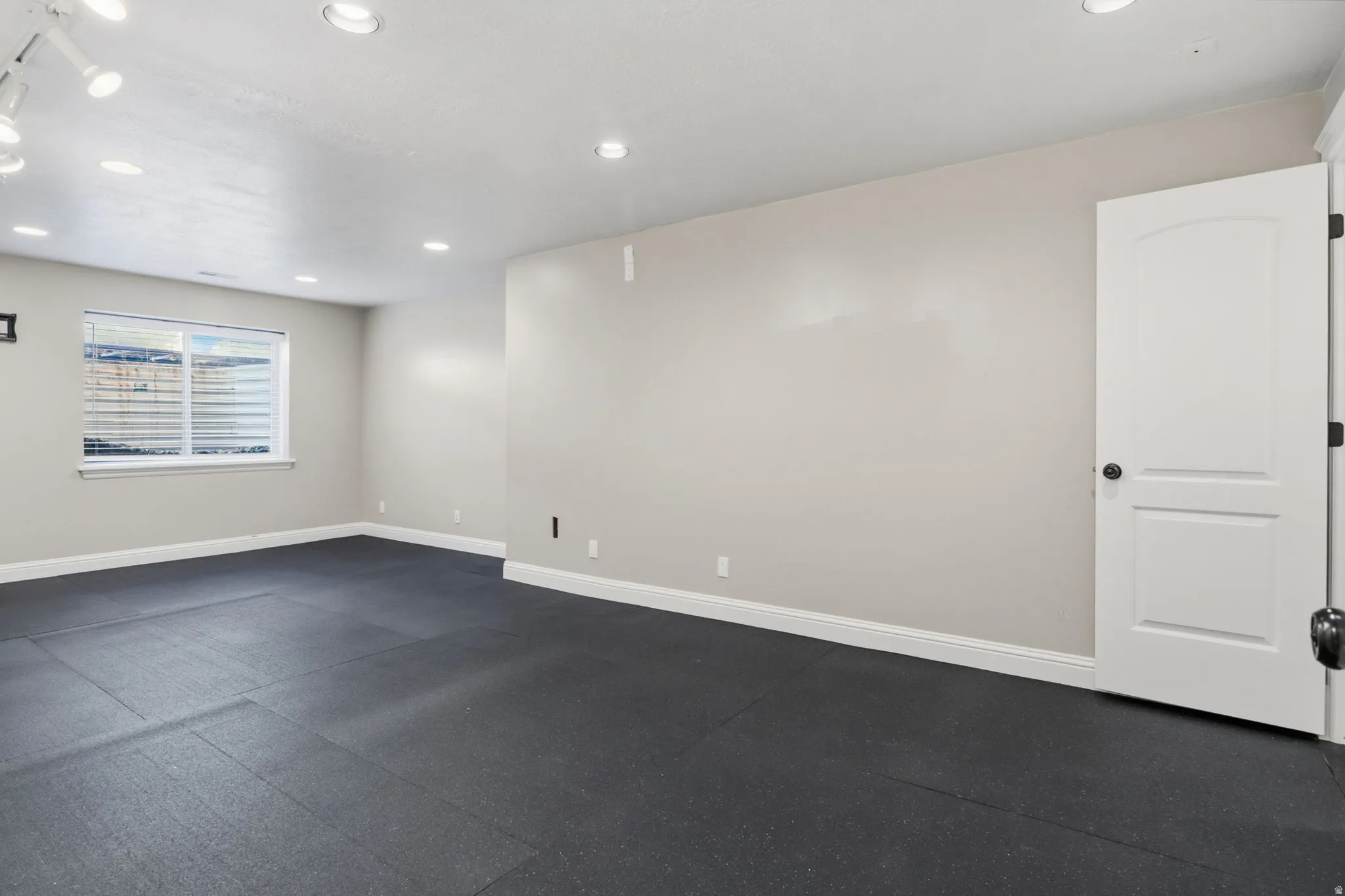 Spacious room featuring dark rubber flooring, light neutral-toned walls, and white baseboards