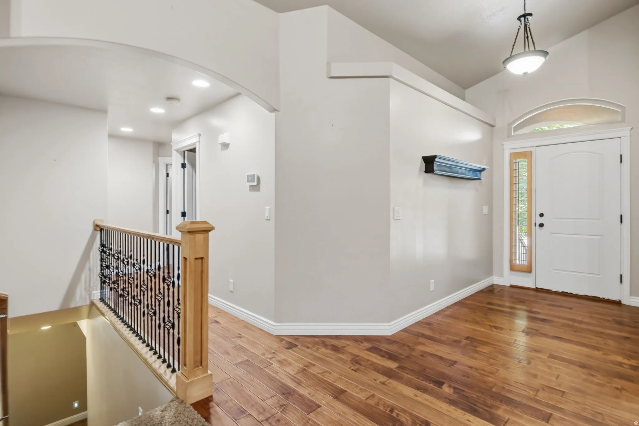 Entryway featuring wood-finish flooring, a white paneled door with sidelight and arched transom, and a pendant light fixture