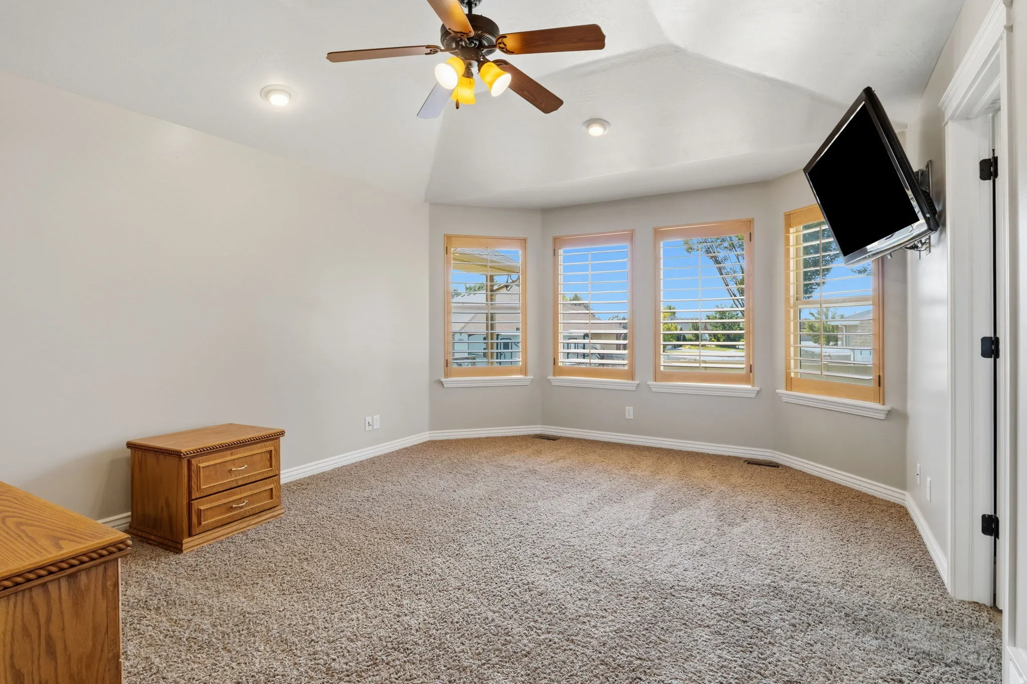 Carpeted room featuring a ceiling fan with integrated lighting, recessed lighting, and a bay window with plantation shutters