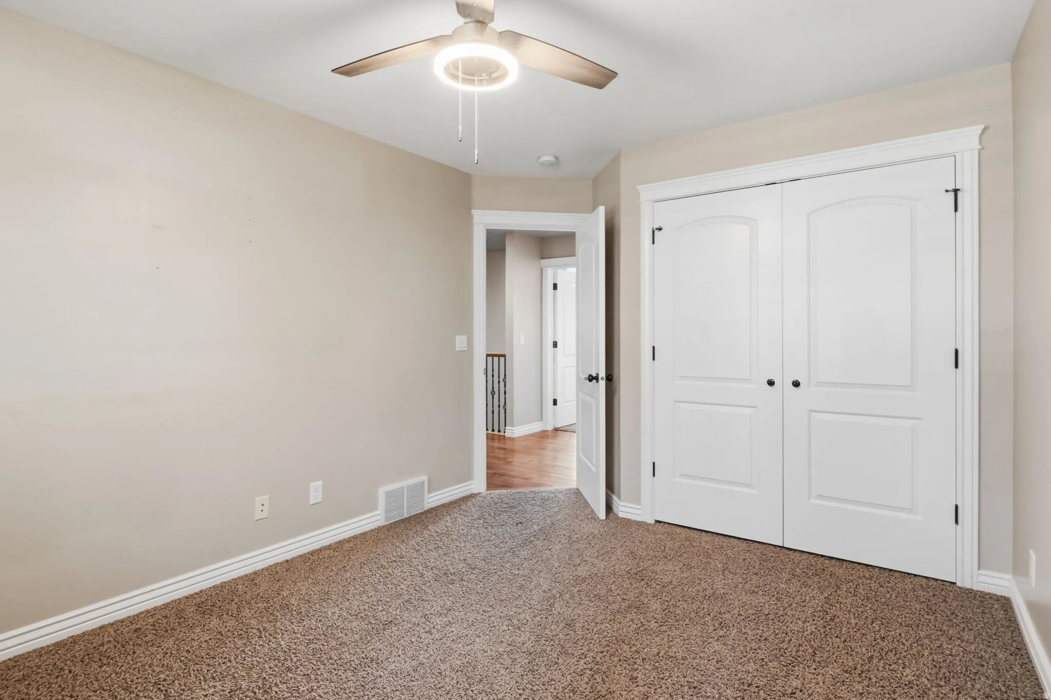 Bedroom featuring neutral carpeting and walls, a ceiling fan with integrated lighting, and white bi-fold closet doors with arched panels