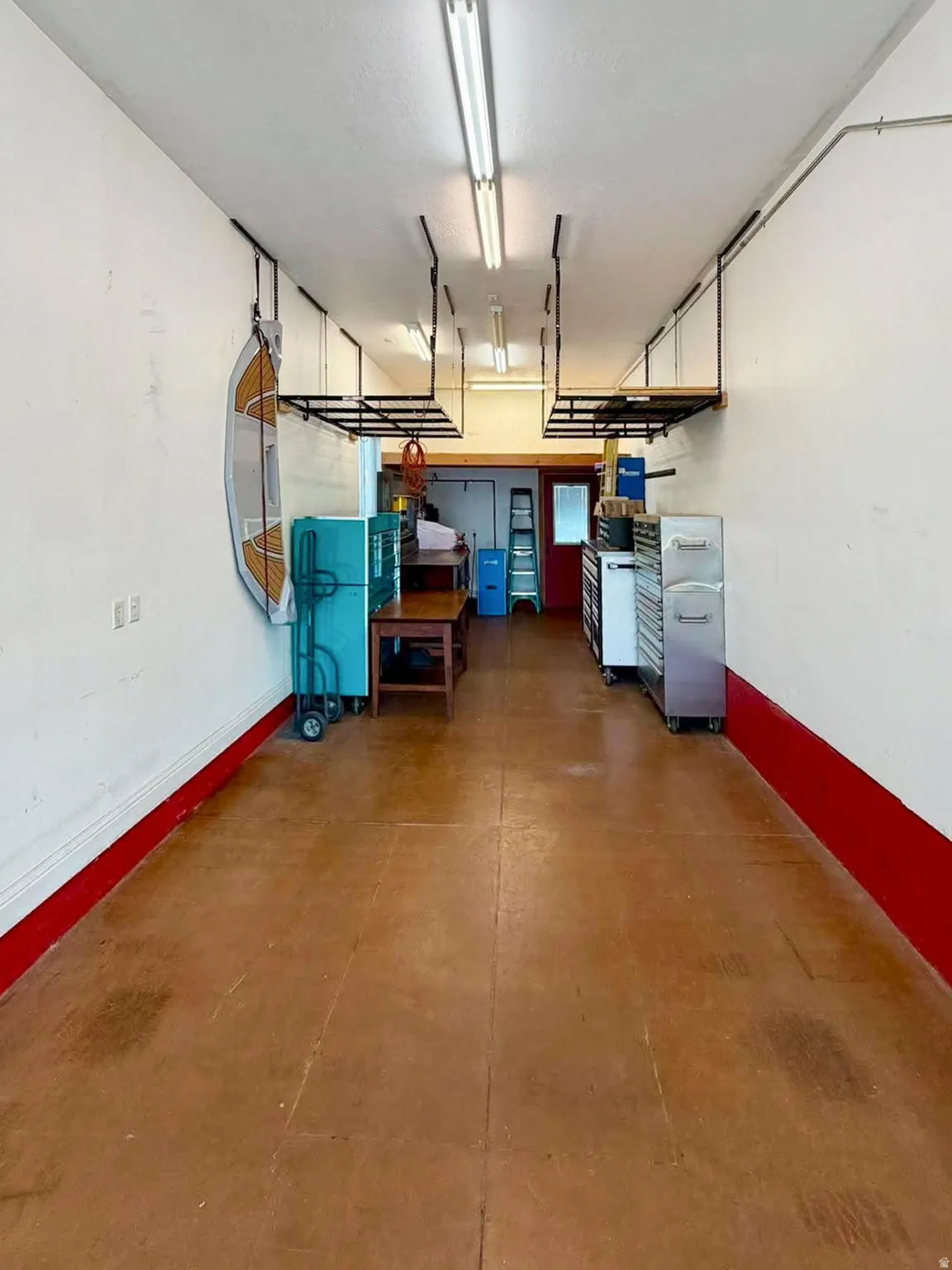 Spacious utility room featuring a concrete floor, white walls with red trim, and multiple fluorescent ceiling light fixtures