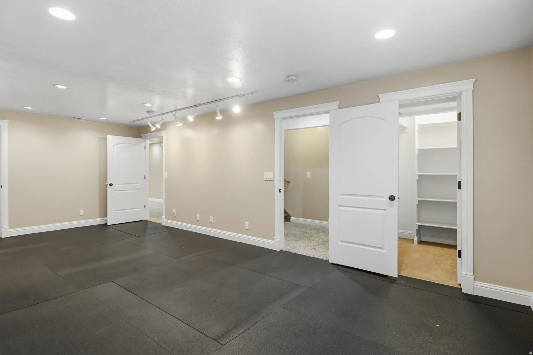 Spacious room featuring dark rubber flooring, recessed lighting, and track lighting