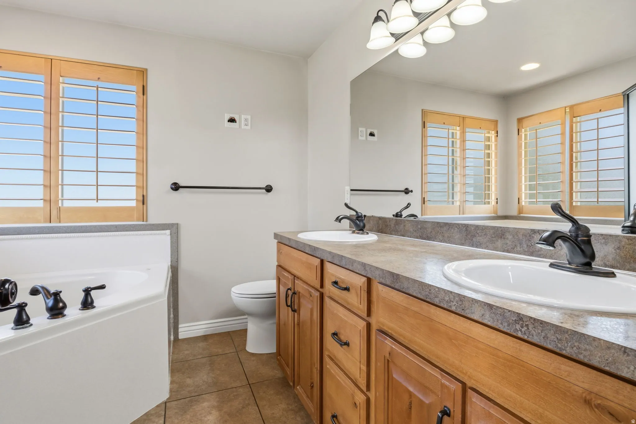 Bathroom featuring a built-in soaking tub with dark bronze fixtures, dual vanity with undermount sinks and dark bronze faucets, wood-finish cabinetry, and neutral-toned countertops