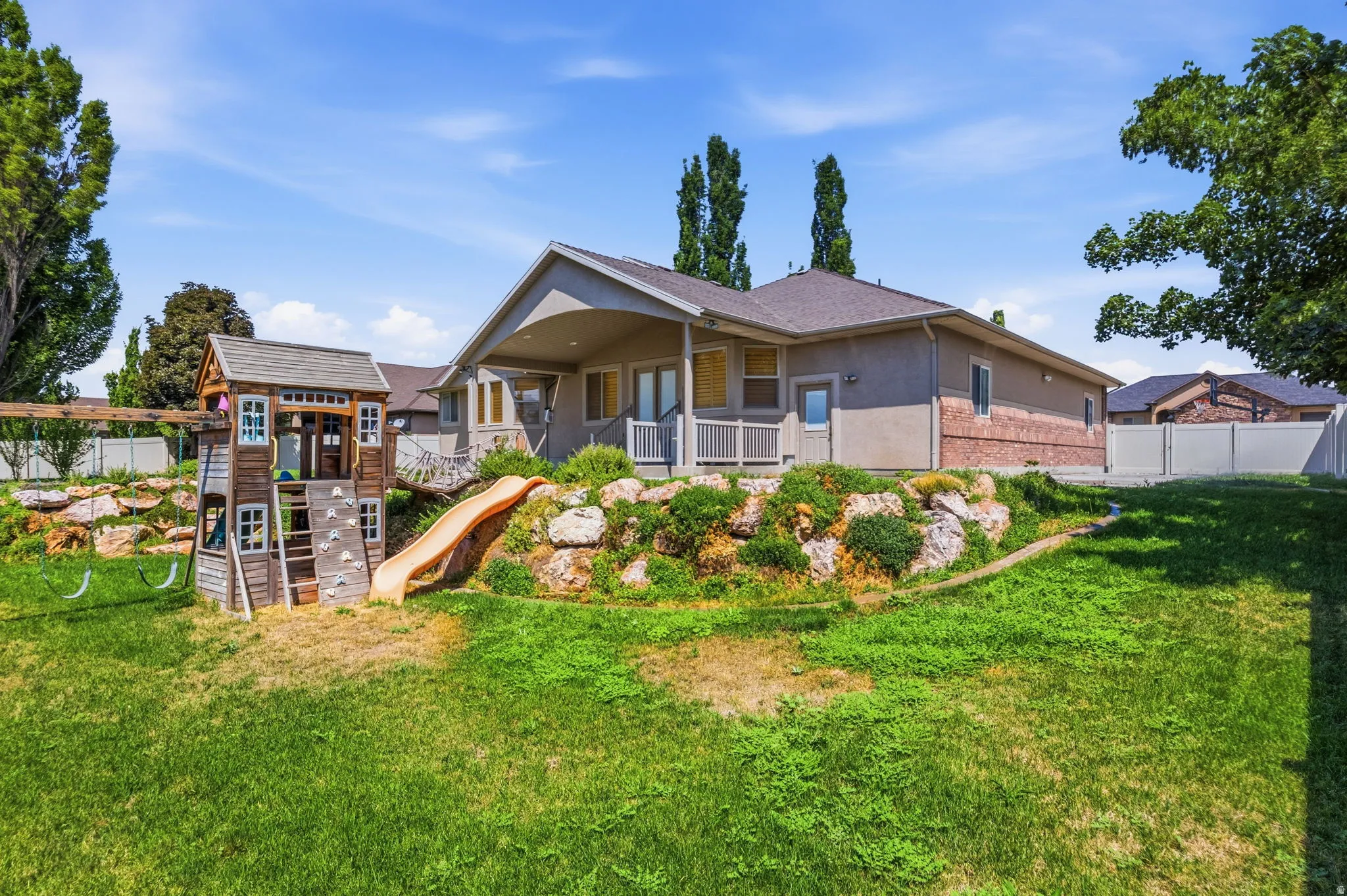 Expansive grassy yard featuring a multi-level wooden playset with swings and a slide
