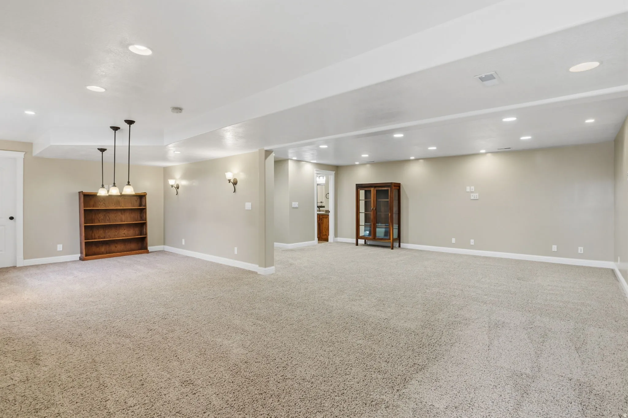 Expansive carpeted area with recessed lighting, pendant light fixtures, and wall sconces
