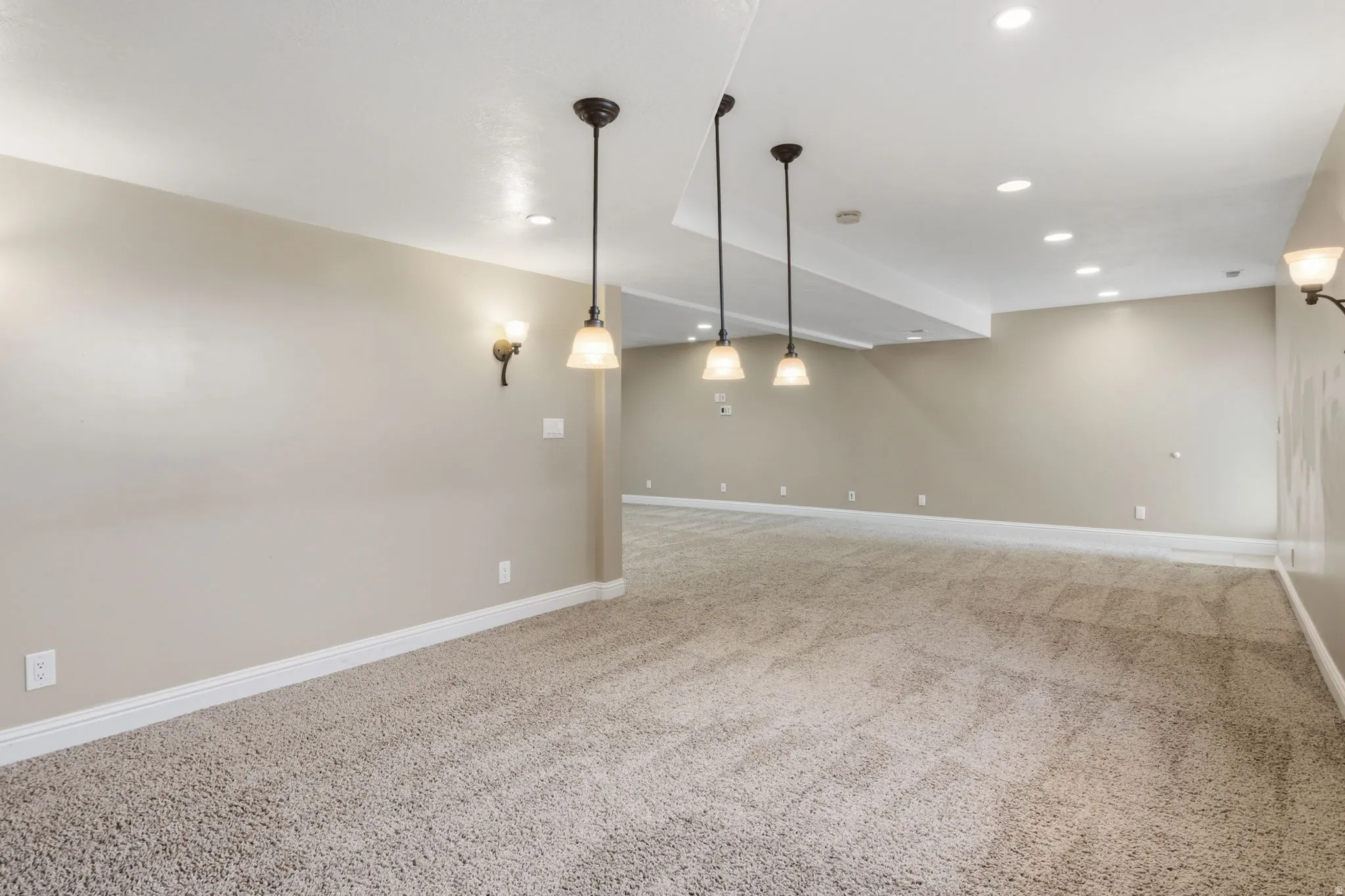 Expansive carpeted area featuring recessed lighting, wall sconces, pendant lights, and neutral-toned walls with white baseboards
