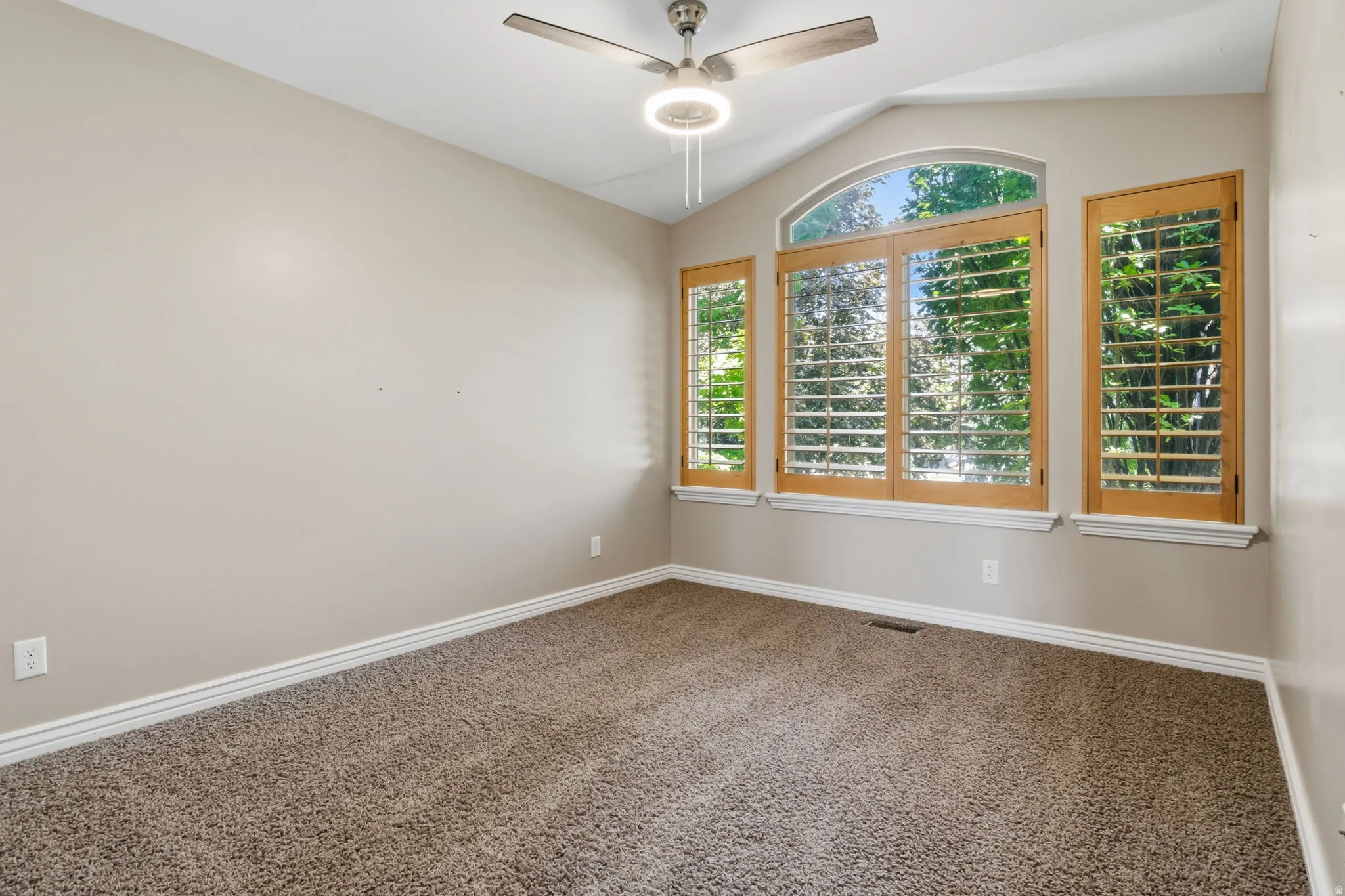Room featuring a vaulted ceiling, wood-finish ceiling fan with integrated lighting, and carpeted flooring