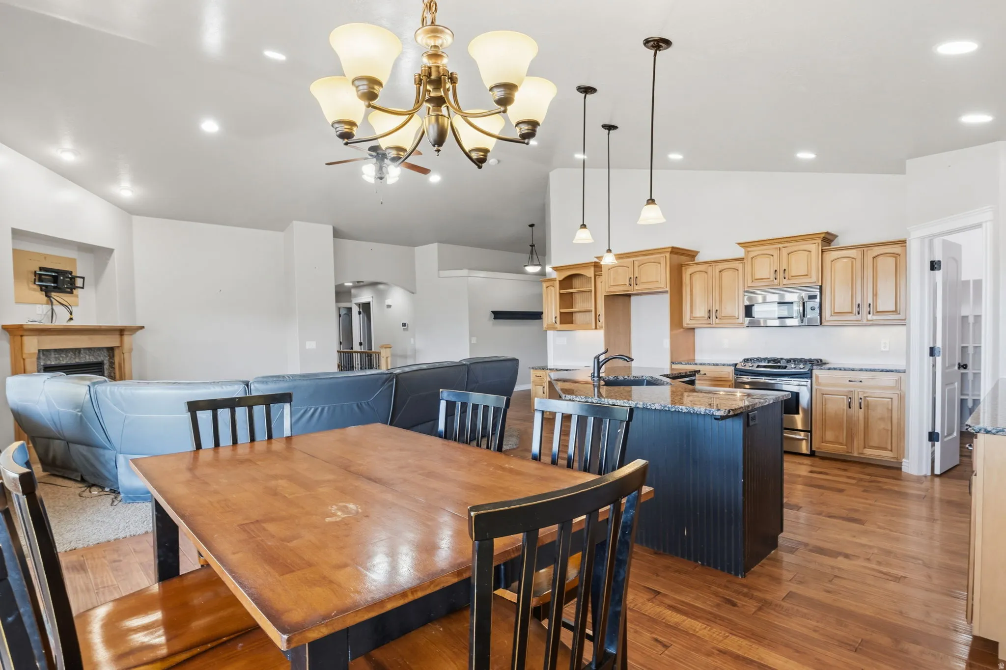 Open-concept interior featuring wood-finish flooring, a kitchen island with pendant lighting, light wood cabinetry, and stainless steel appliances