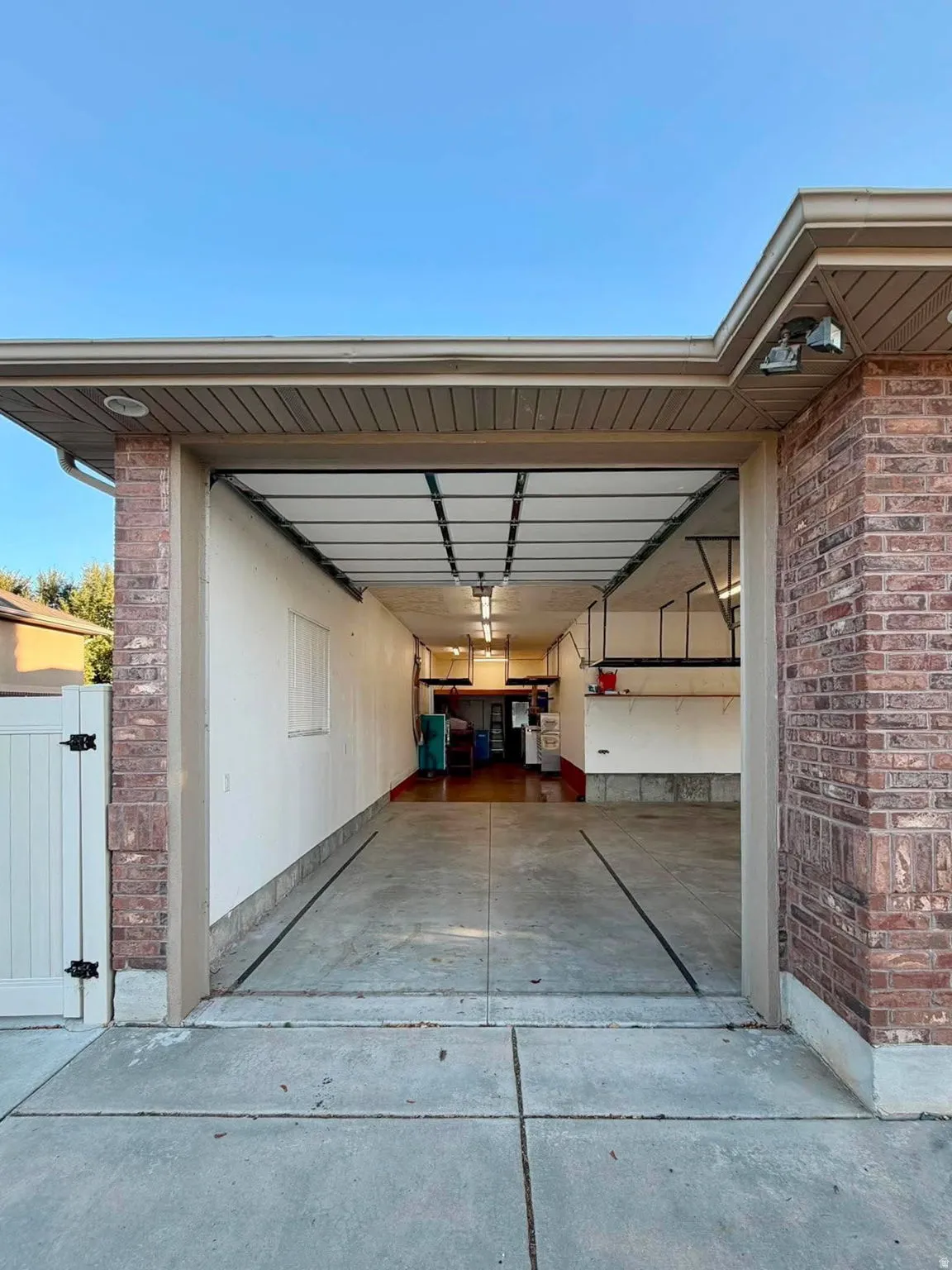 Brick exterior with a roll-up garage door, concrete driveway, and white privacy fence