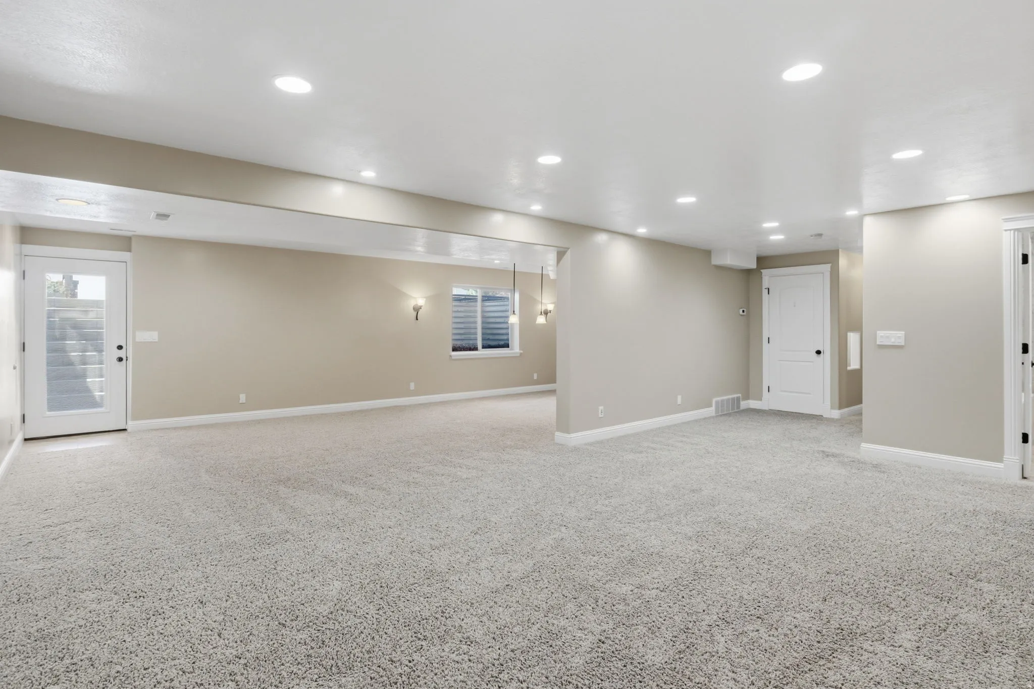 Spacious interior featuring light gray carpeting, recessed ceiling lighting, a full-light exterior door, and a horizontal window with blinds