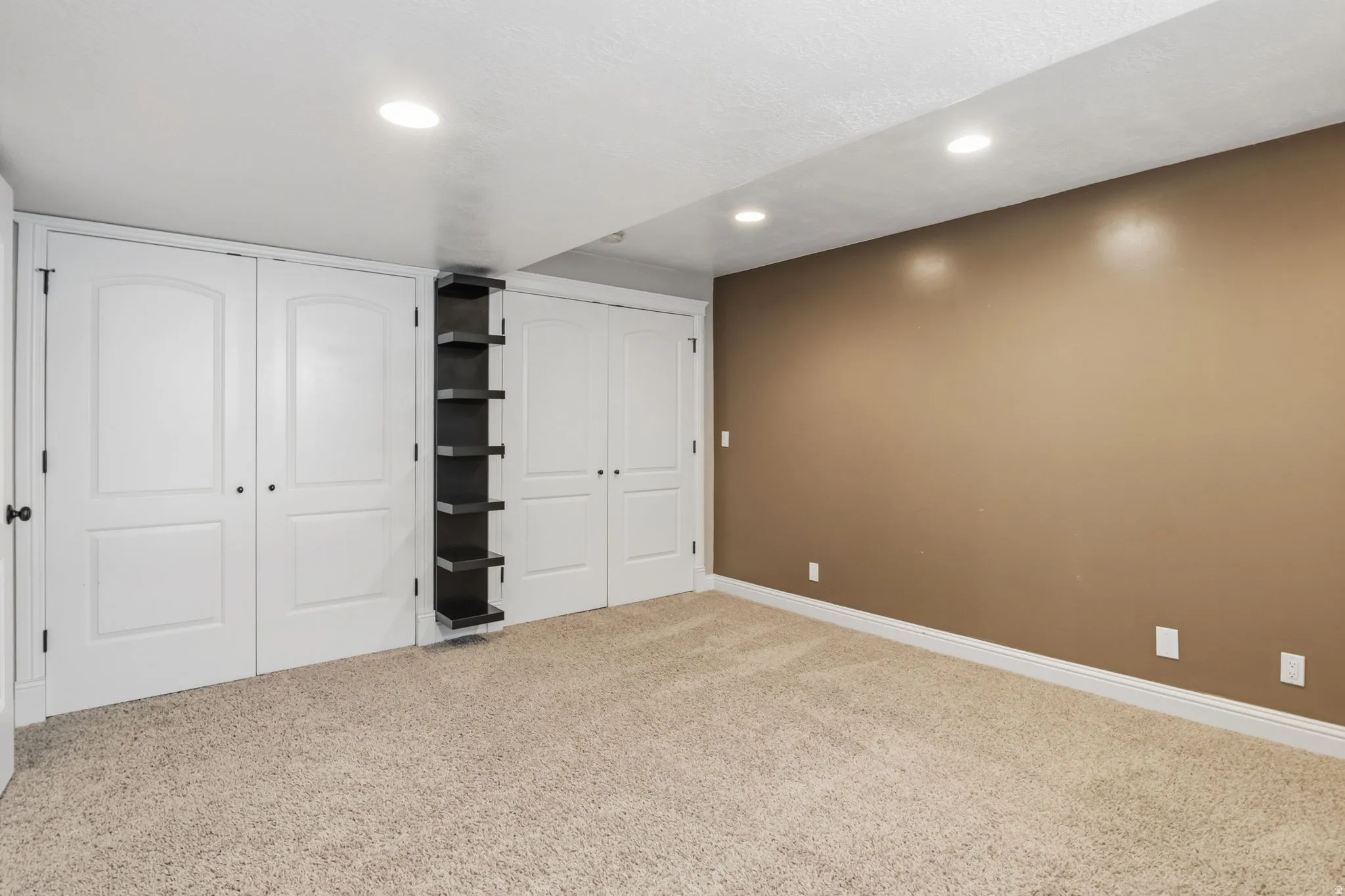 Spacious room featuring neutral carpeting, a warm accent wall, and multiple recessed ceiling lights
