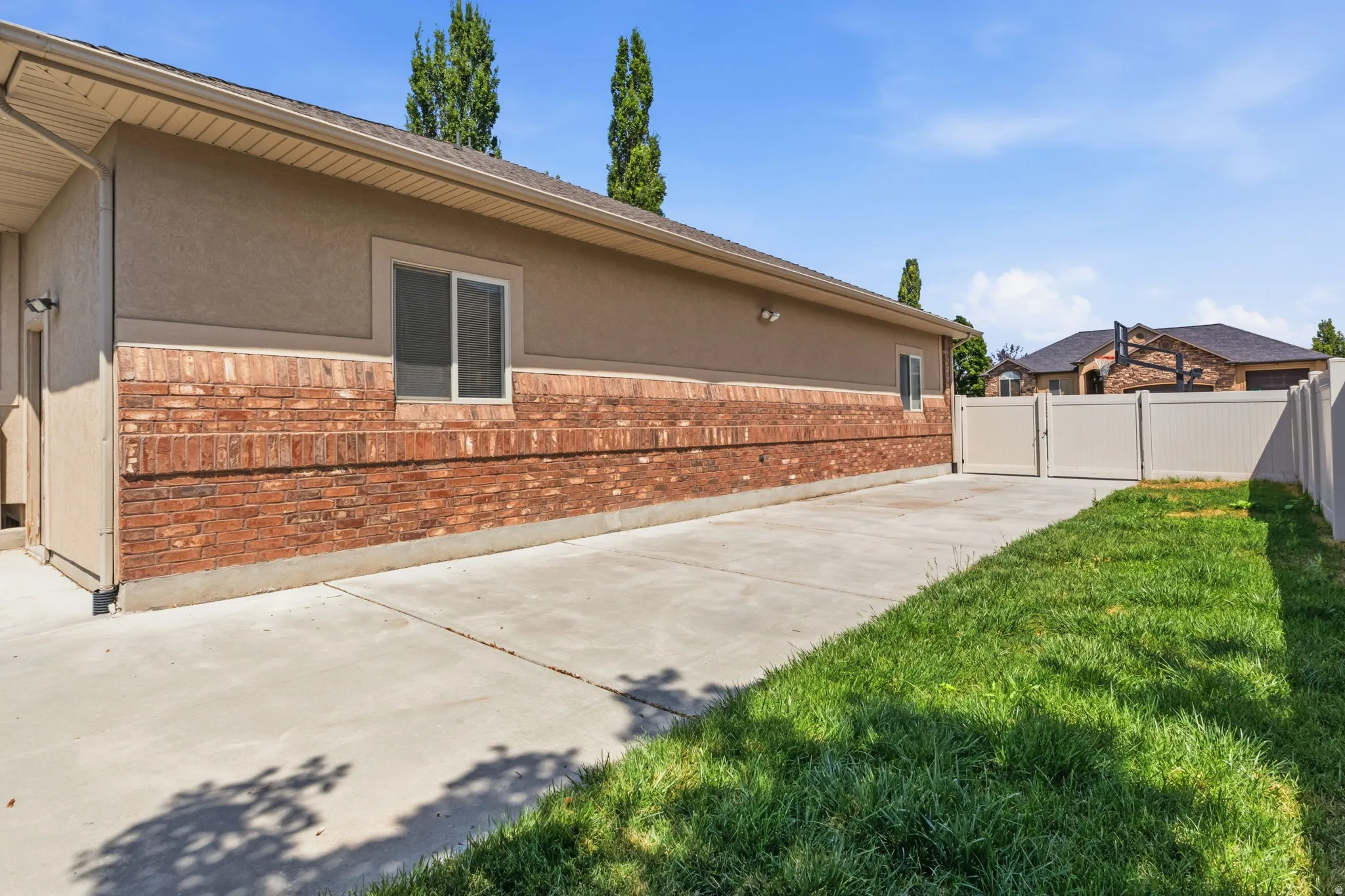 Exterior featuring a concrete driveway, brick and stucco siding, a white privacy fence, a grass lawn, and multiple windows