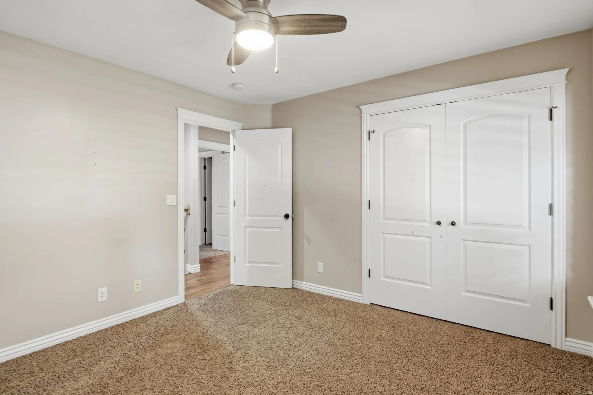 Interior room featuring neutral wall paint, carpet flooring, a ceiling fan with integrated lighting, and white bi-fold doors