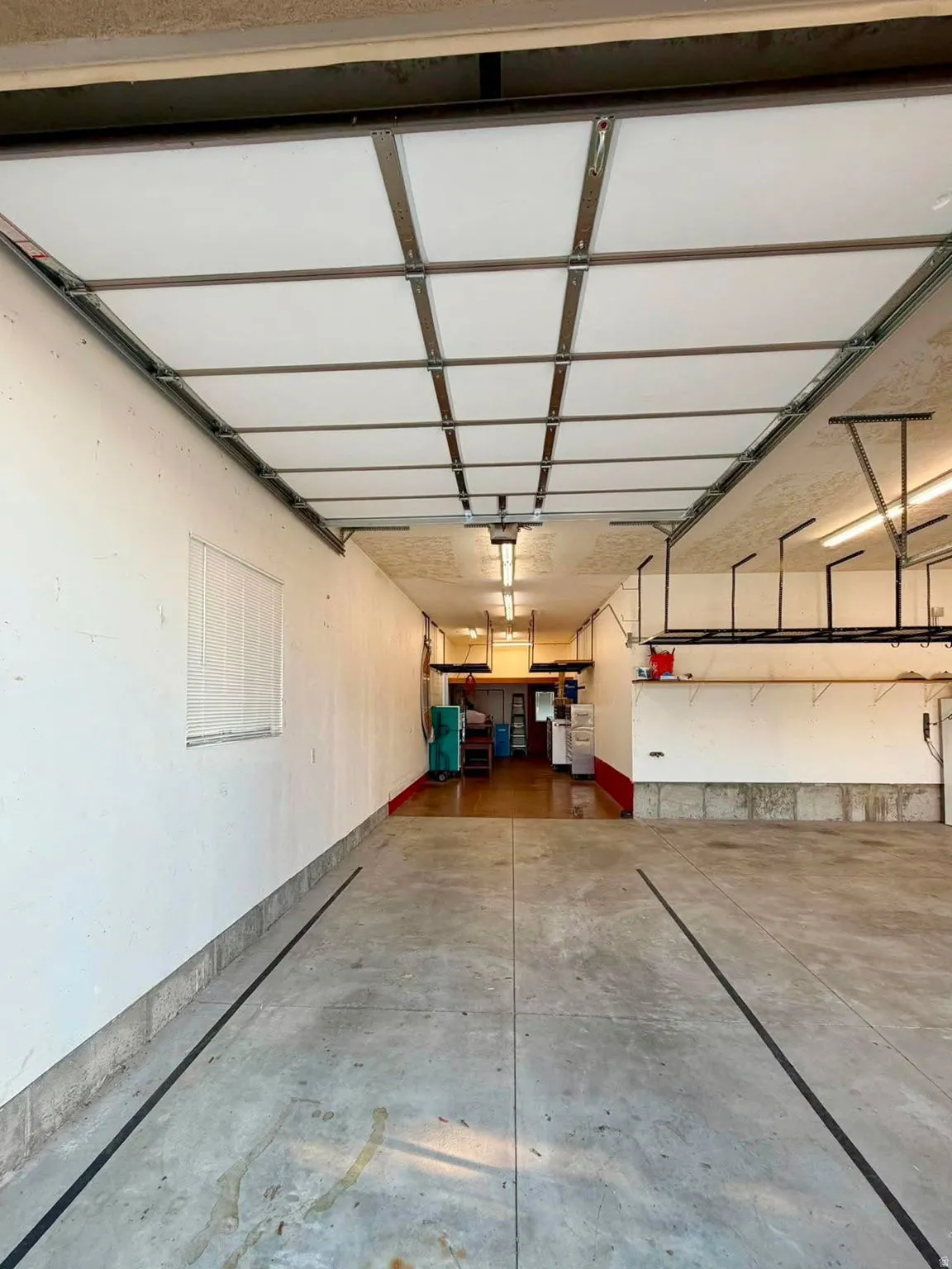 Spacious garage with concrete flooring, overhead fluorescent lighting, and a window with blinds