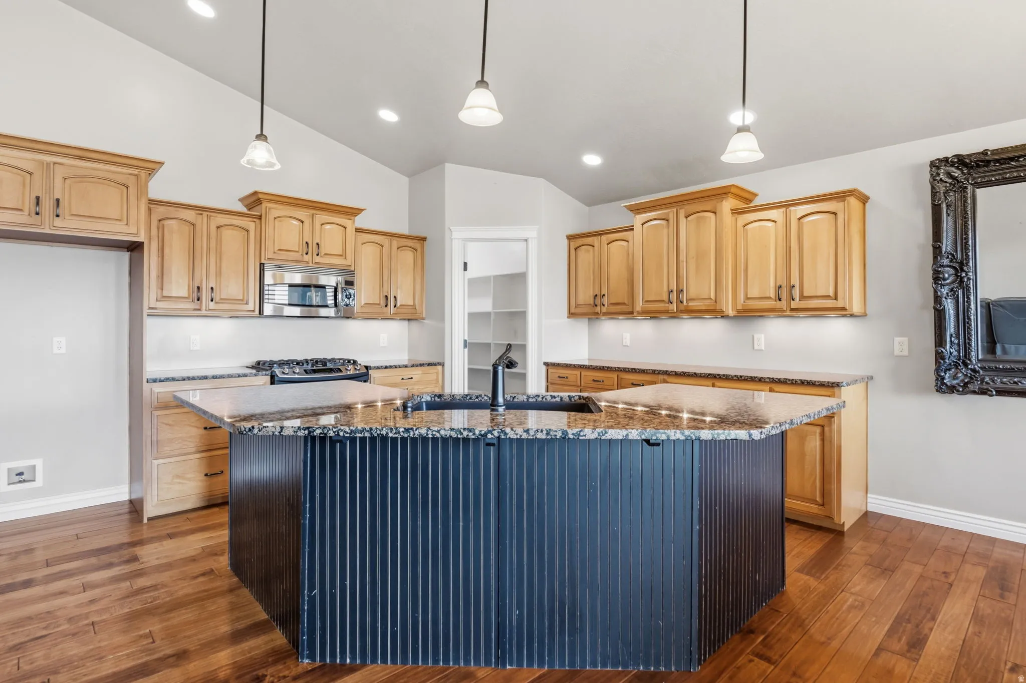 Kitchen featuring a large multi-sided island with a built-in sink, wood-finish flooring, light wood cabinetry, granite countertops, and stainless steel appliances