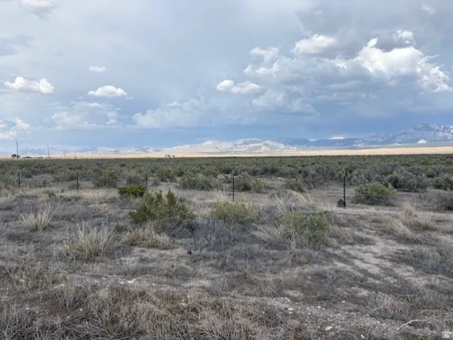 Expansive land parcel featuring natural desert vegetation, partial fencing, distant mountain ranges, and a vast open sky