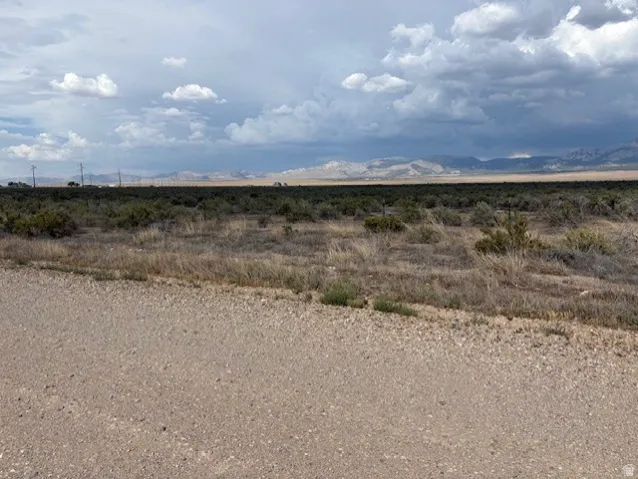 Expansive open land featuring natural desert vegetation, a gravel road, and distant mountain ranges