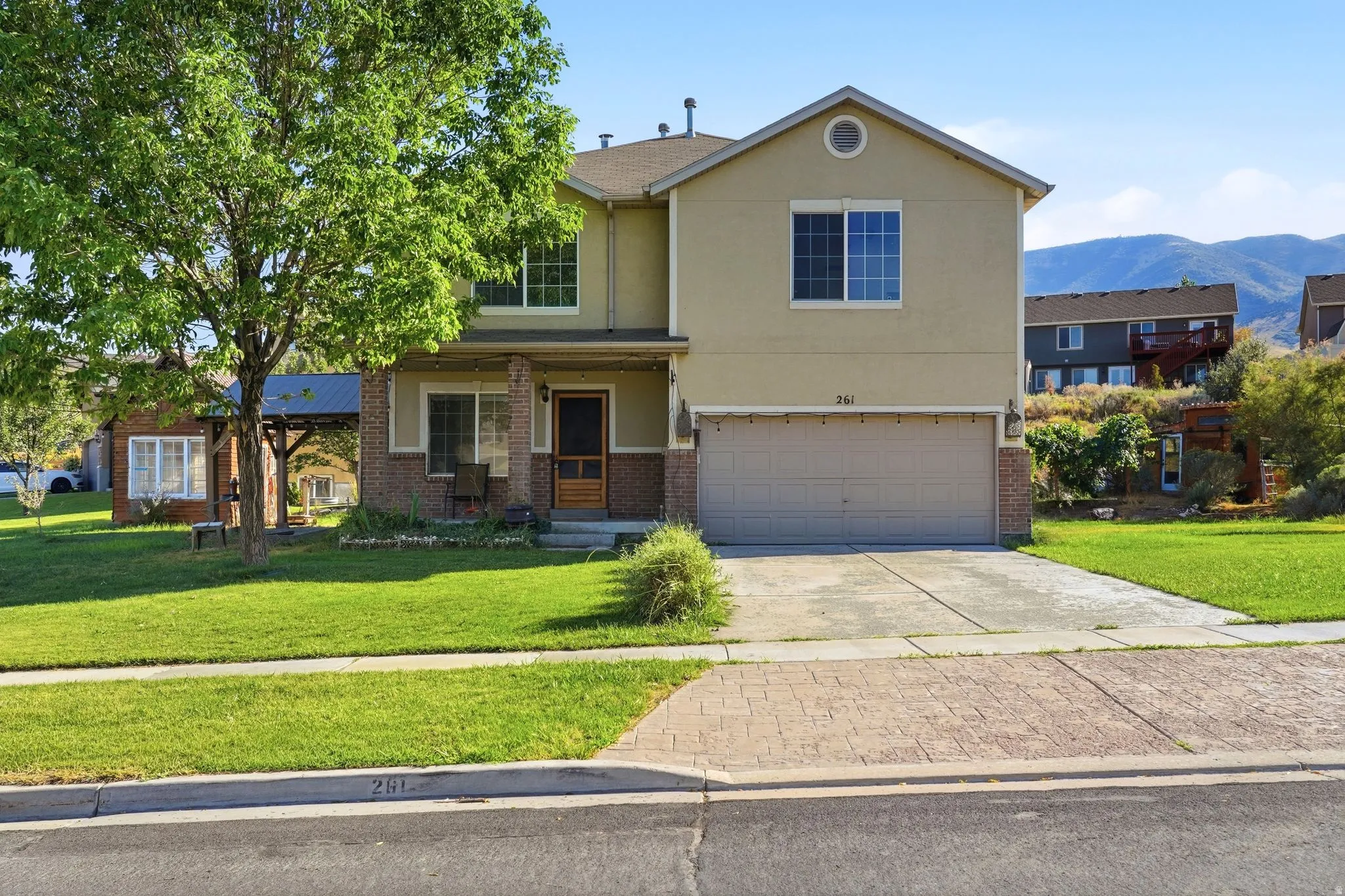 Two-story stucco and brick exterior featuring a covered porch, an attached two-car garage, and a lush green lawn