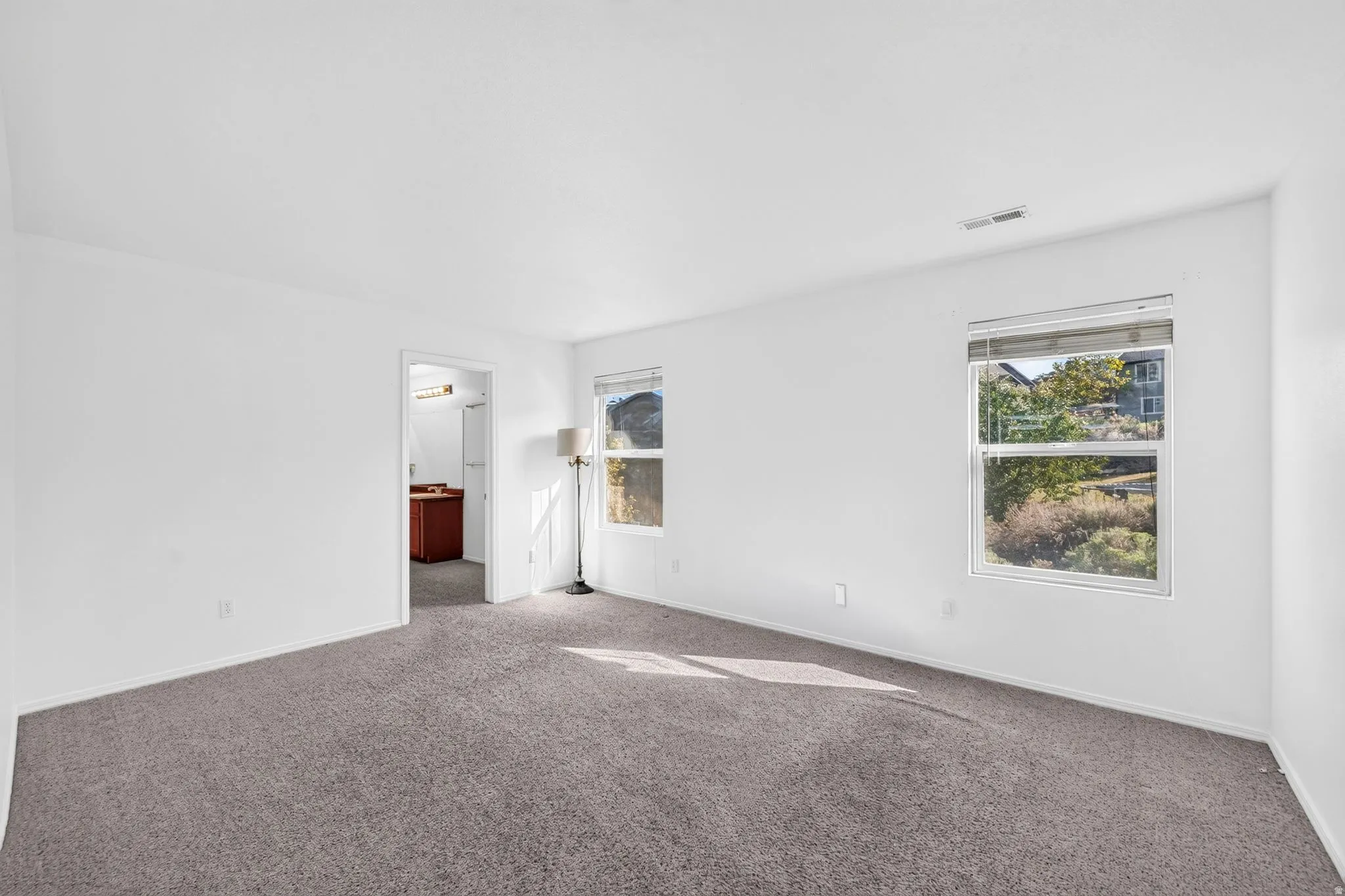 Carpeted room with white walls, two single-hung windows, and a doorway opening into a room with a dark wood-finish vanity