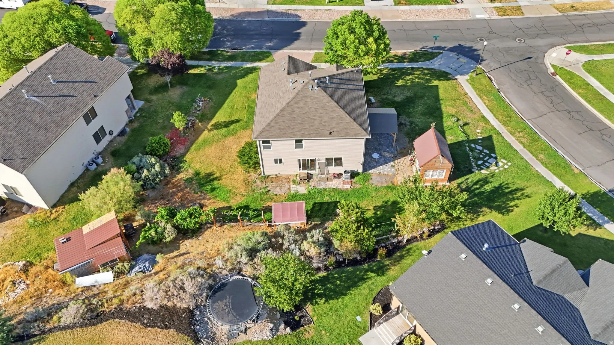 Expansive property featuring a two-story residence with a tan exterior and brown roof, a detached shed with a brown roof, mature landscaping, a paved patio area, and a green lawn