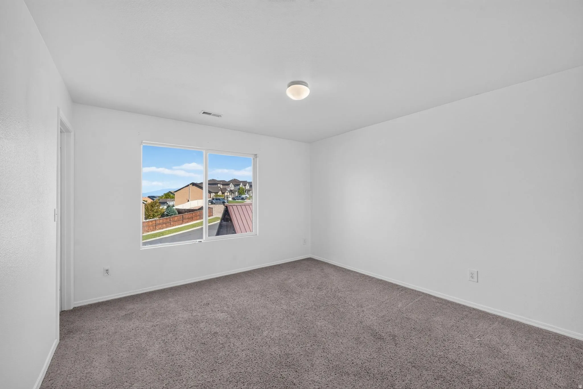 Light-filled room featuring a large window, neutral gray carpeting, white walls, a flush-mount ceiling light, and a white trim package