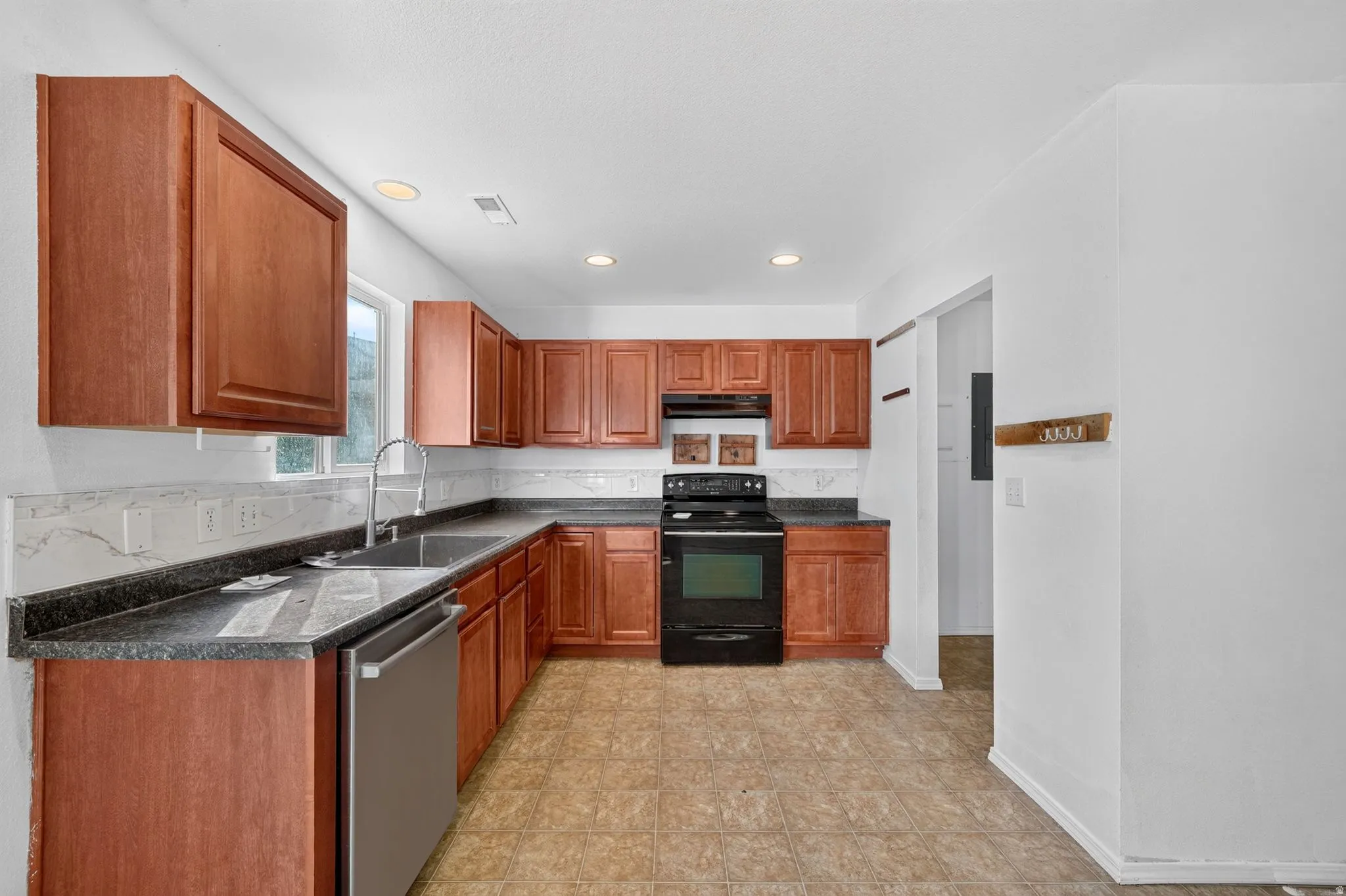 Kitchen featuring wood cabinetry, dark countertops, a stainless steel sink with a high-arc faucet, a black range, and tile flooring