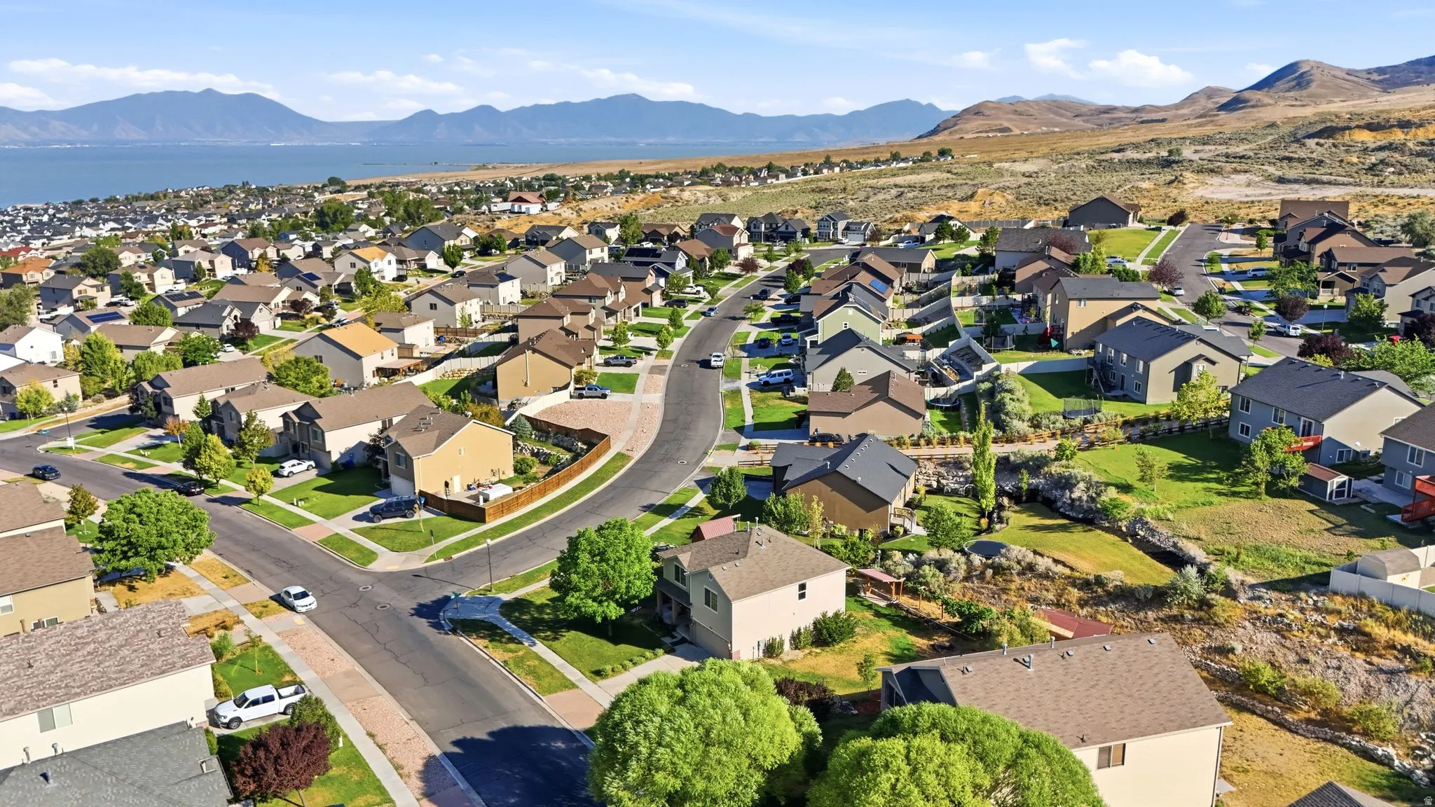 Expansive neighborhood featuring varied residential architecture, mature landscaping, paved roads, and distant mountain and water scenery