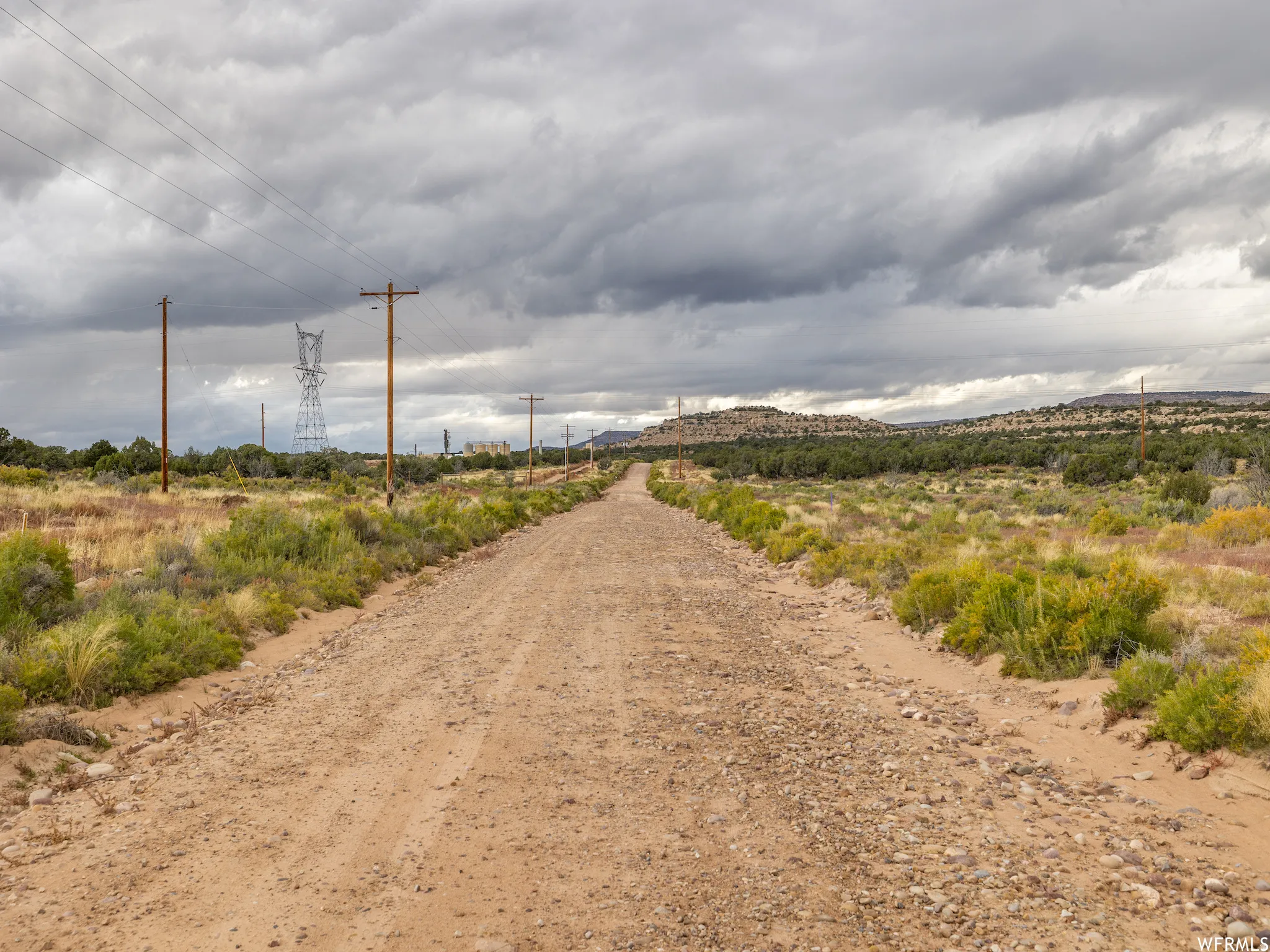 Gravel road traversing natural desert foliage with distant utility infrastructure and hills