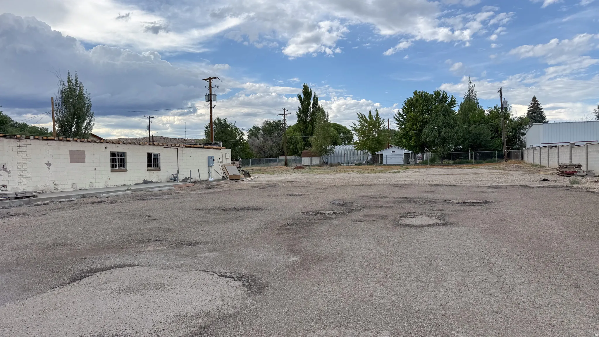 Expansive paved lot with mature trees and a partial white brick structure