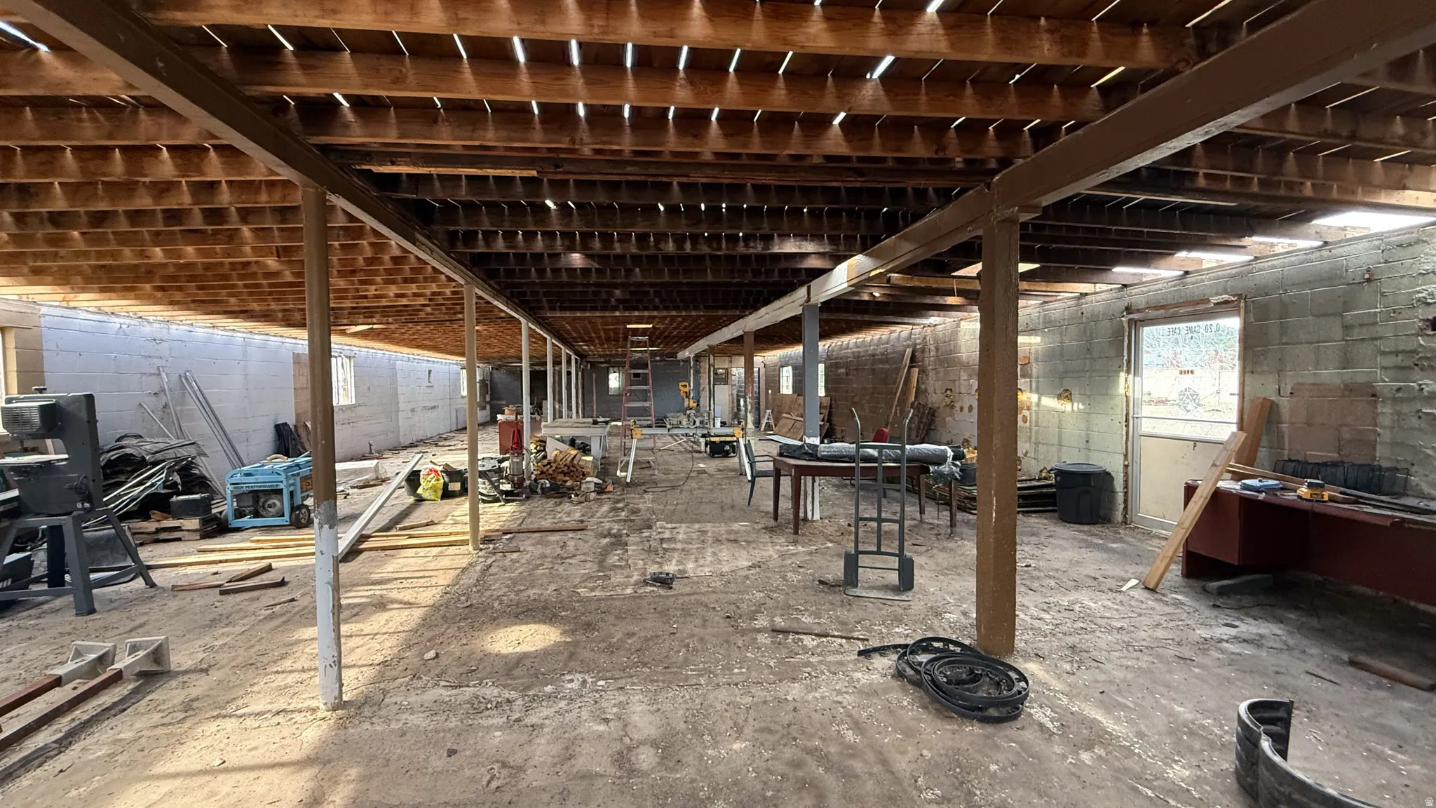 Spacious unfinished lower level featuring exposed wood joists and support beams, concrete block walls, multiple windows, and a rear door entry