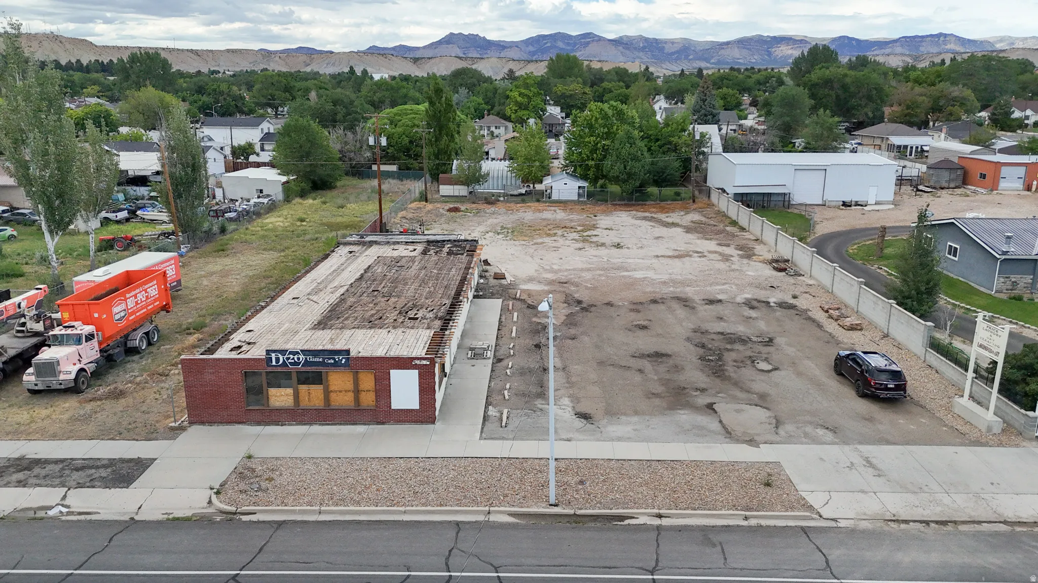 Brick-front commercial building with street frontage, an expansive unpaved lot, and surrounding mountain backdrop