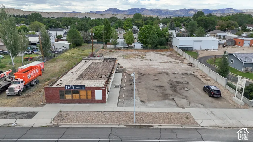 Brick-front commercial building with street frontage, an expansive unpaved lot, and surrounding mountain backdrop