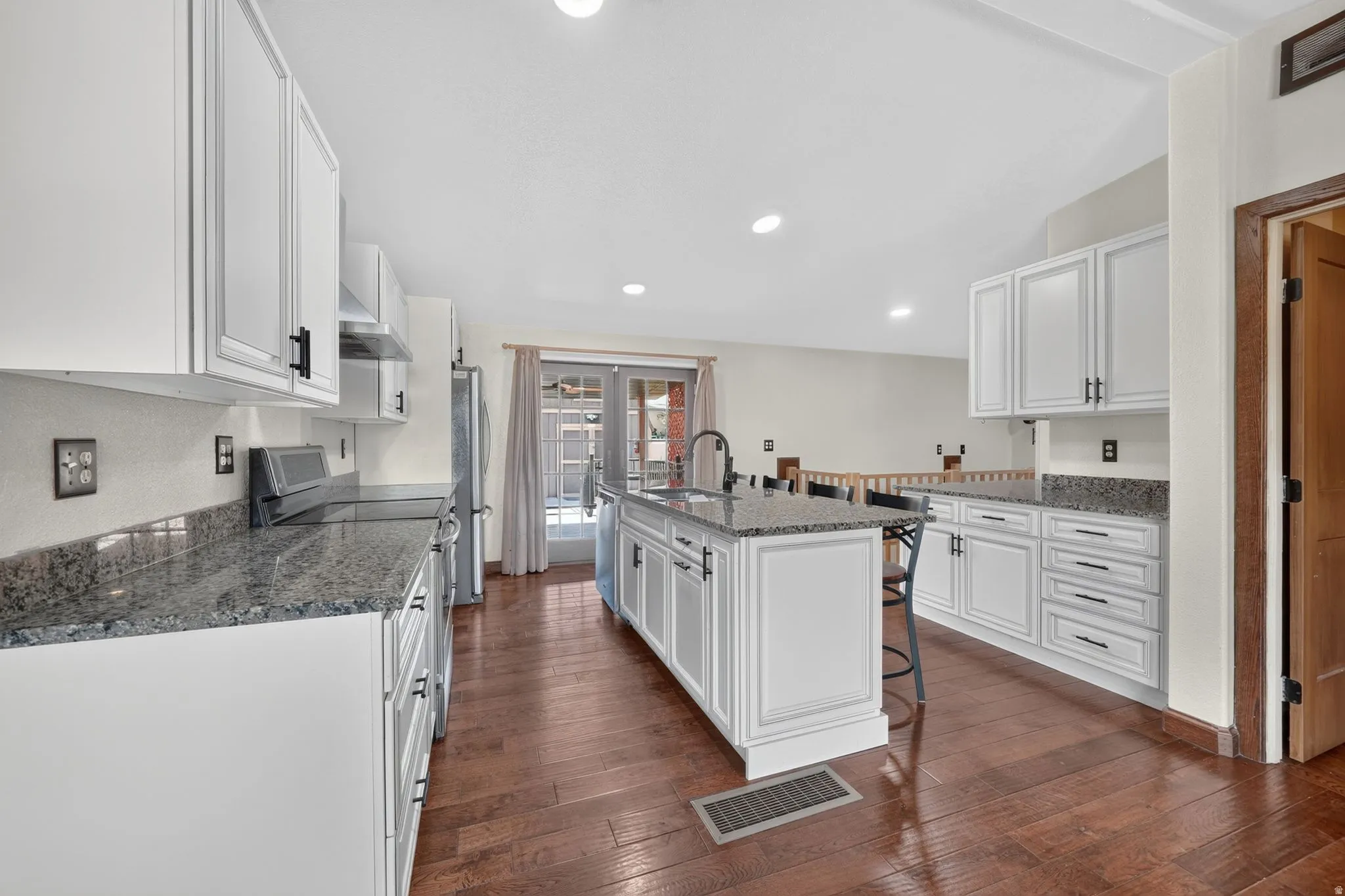 Kitchen featuring an island with seating, white shaker cabinetry, speckled countertops, stainless steel appliances, and wood-finish flooring