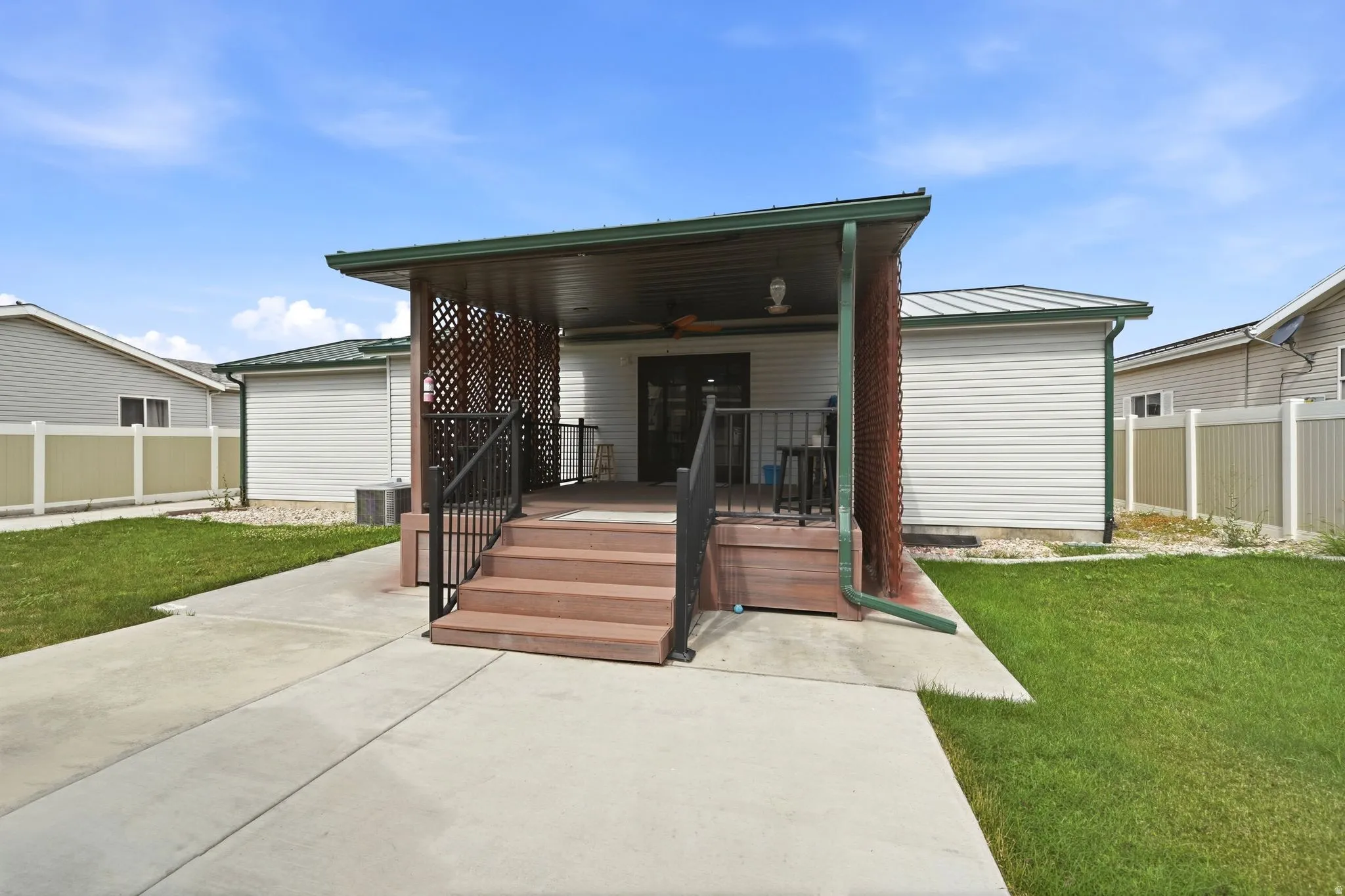 Rear exterior featuring a covered porch with lattice-work privacy screens, wood-finish decking, and black metal railings