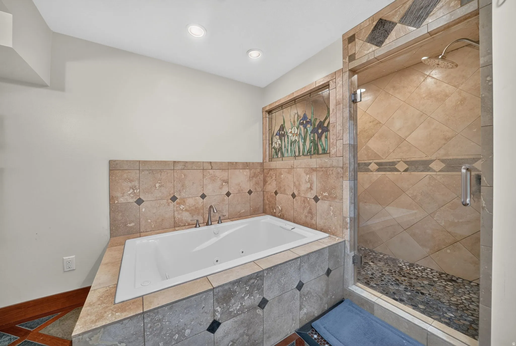 Spa-like bathroom with jetted tub, custom tile work, glass-enclosed shower, rain shower head, and decorative stained-glass accent
