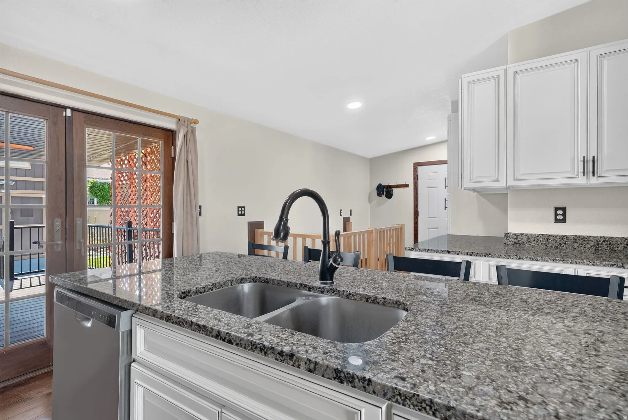 Kitchen island featuring a double basin stainless steel sink with a matte black high-arc faucet, granite countertops, and white cabinetry