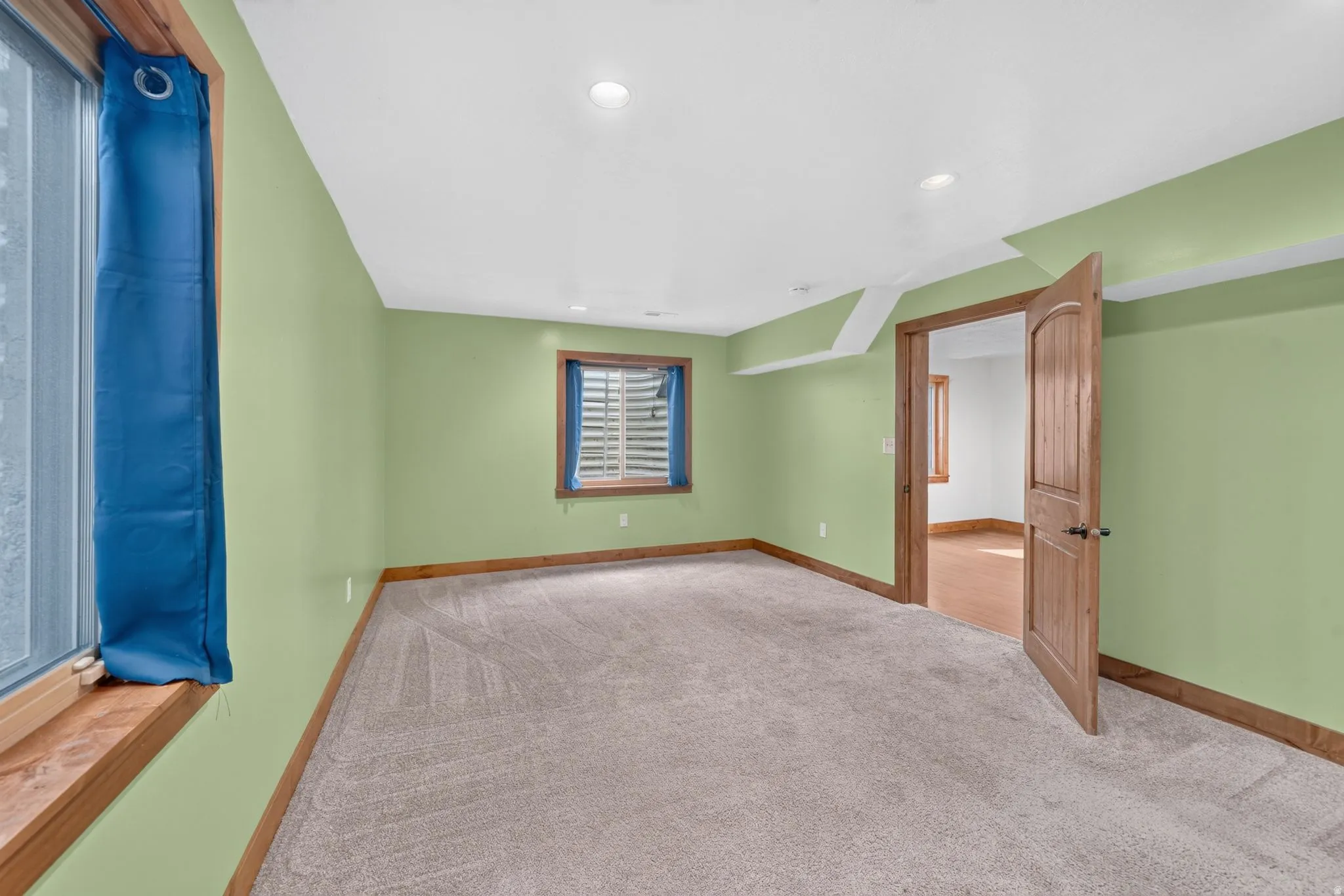Spacious room featuring light green walls, light-colored carpeting, and recessed lighting