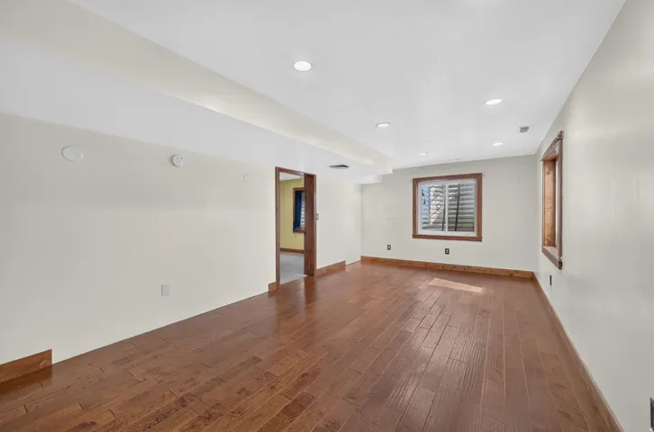 Spacious room featuring wood-finish flooring, recessed lighting, neutral wall tones, and wood-trimmed windows
