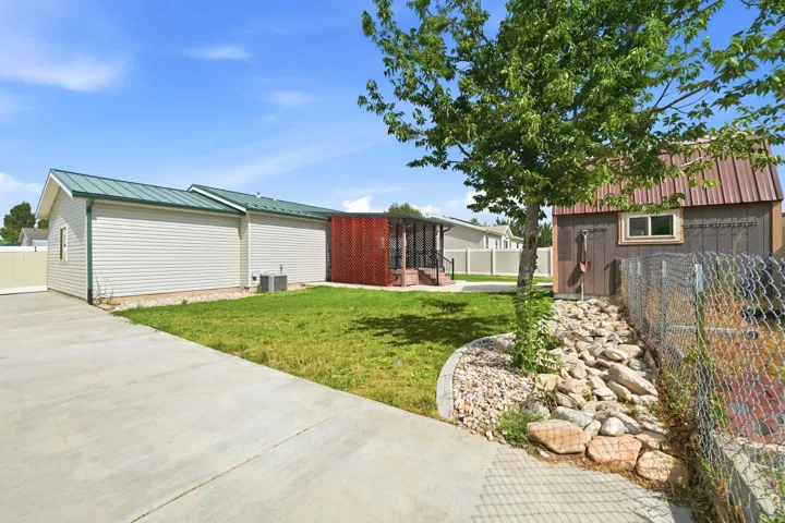 Concrete driveway and walkway with a manicured lawn, accent tree, and a storage shed featuring a metal roof