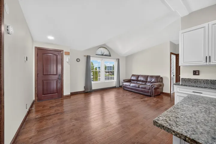 Spacious living area featuring wood-finish flooring, vaulted ceilings, and a large window with an arched transom