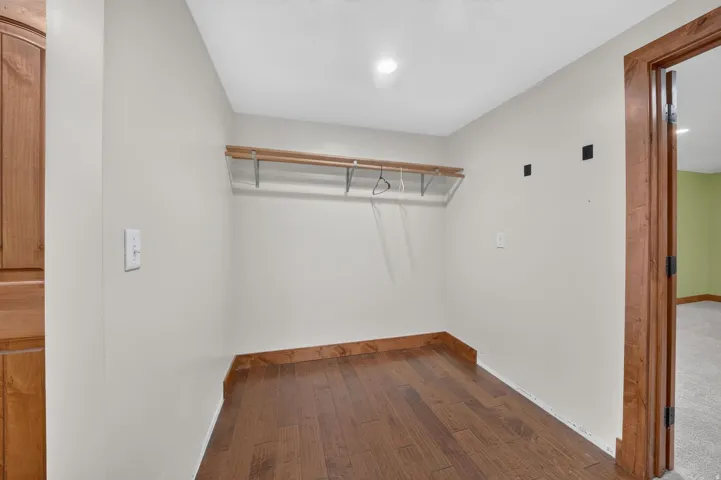 Closet space featuring wood-finish flooring, a built-in hanging rod, and light neutral wall paint