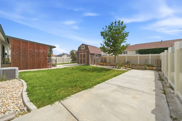Landscaped backyard featuring a storage shed with a brown metal roof, a concrete pad, a manicured lawn, and a privacy fence