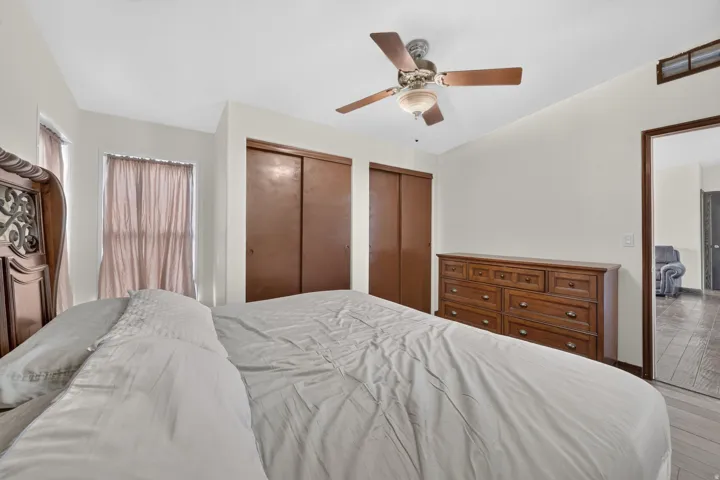 Bedroom featuring neutral wall colors, wood-finish flooring, two sliding closet doors, and a ceiling fan with integrated lighting